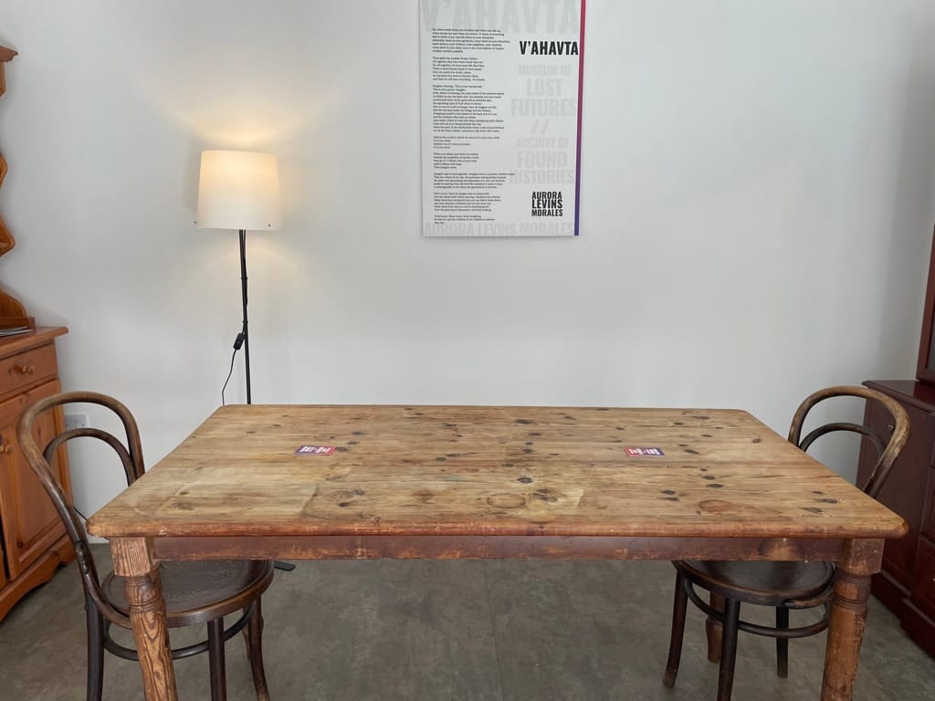 A dining table sat in front of a lamp and a board showing the Aurora Levins Morales poem "V'ahavta".