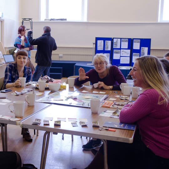 A group of people gathered around a table in a town hall, playing a game.