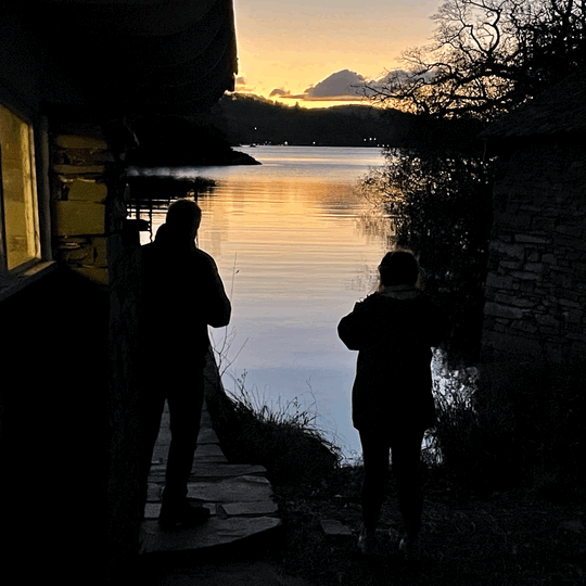 An image of two people standing in front of a lake at sunrise.