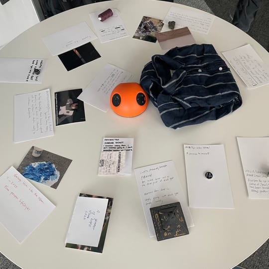 A round table with items on it. Each item has a handwritten museum placard. The items include clothing, esotera, photos.